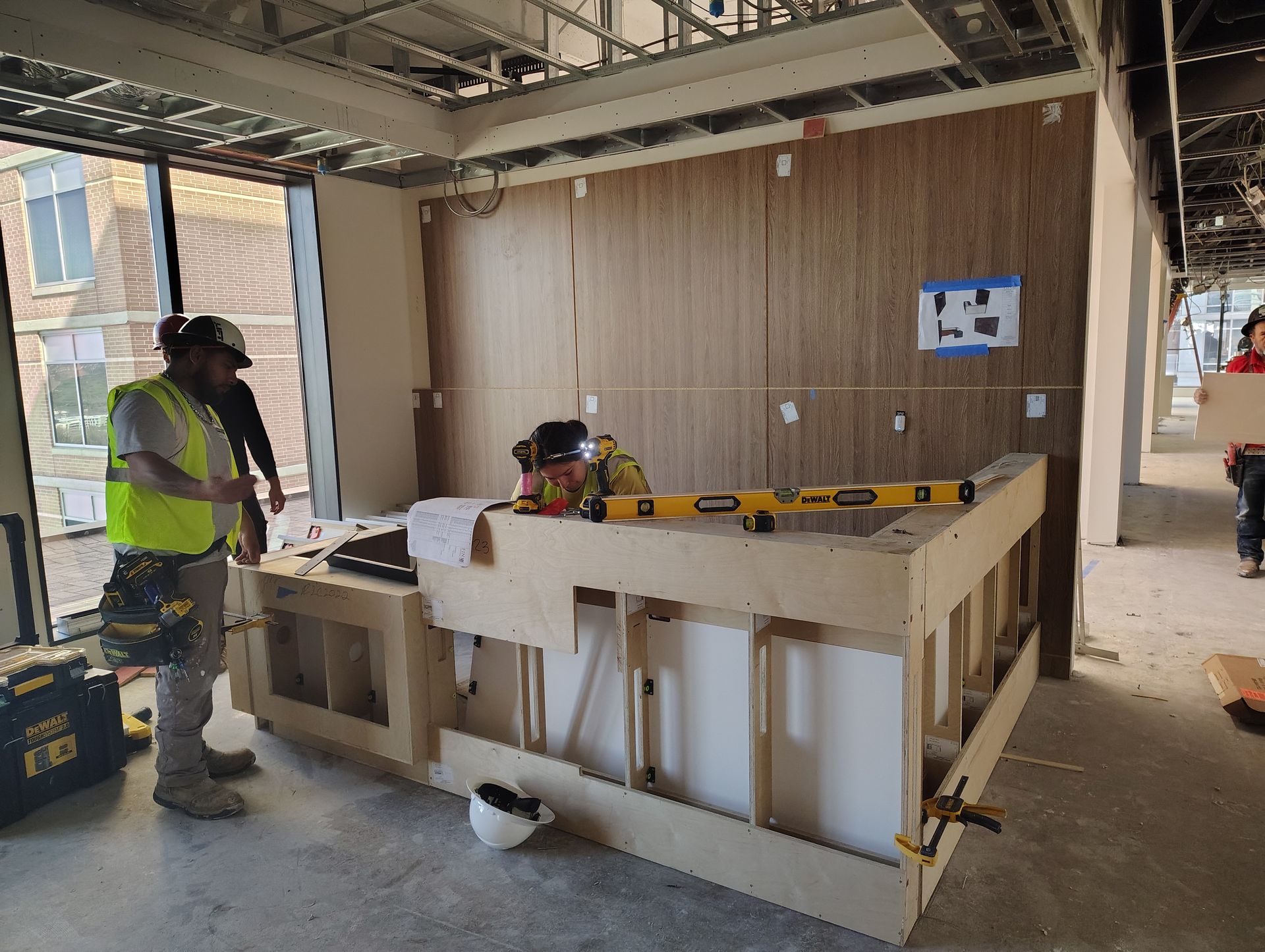Two construction workers are working on a wooden counter in a building under construction.