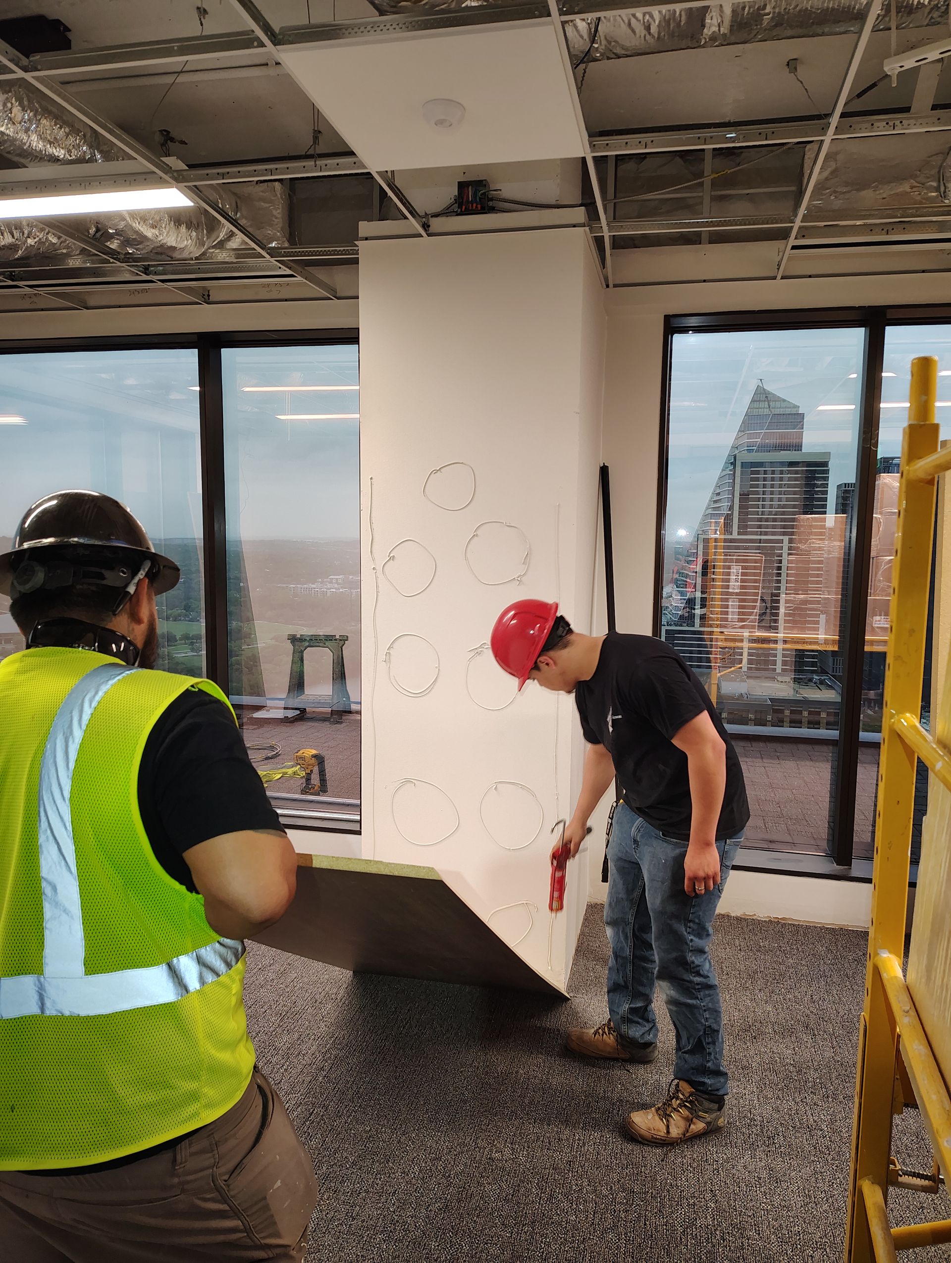 Two construction workers are working on a wall in a building.