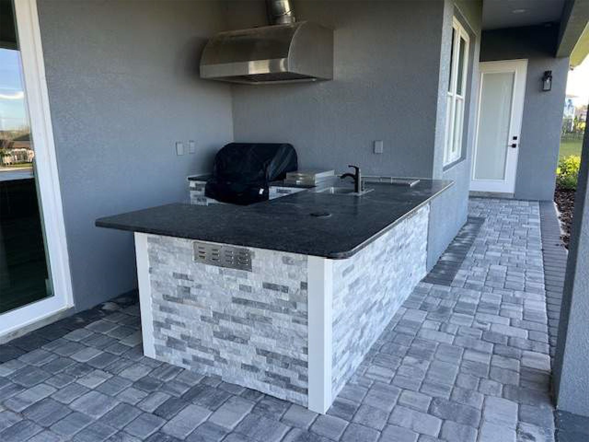 An outdoor kitchen with a grill and a sink on a brick patio.