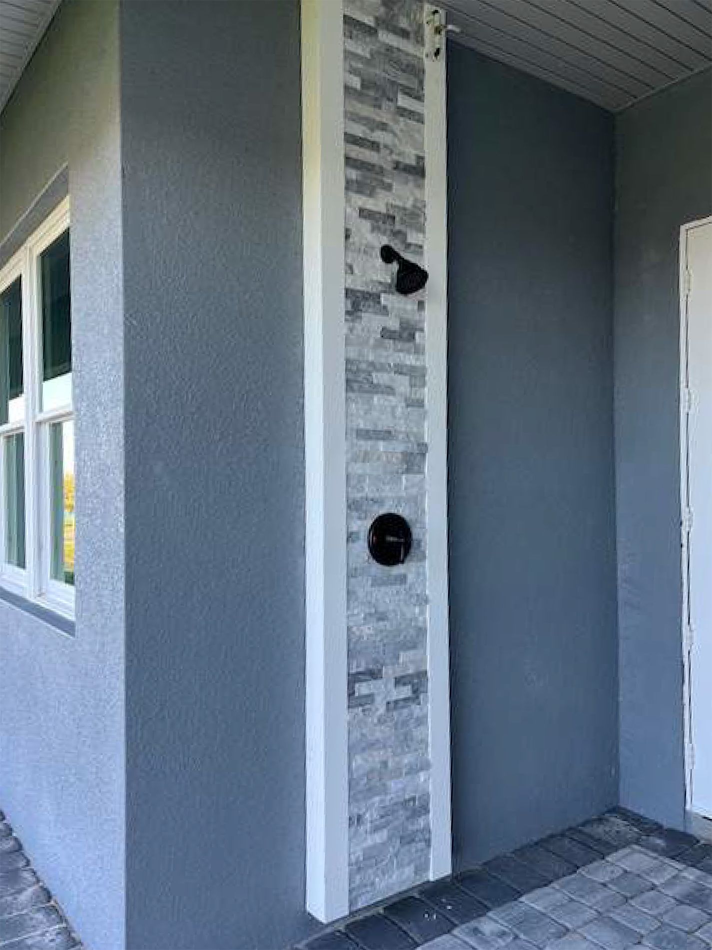 A gray house with a white door and a brick wall.
