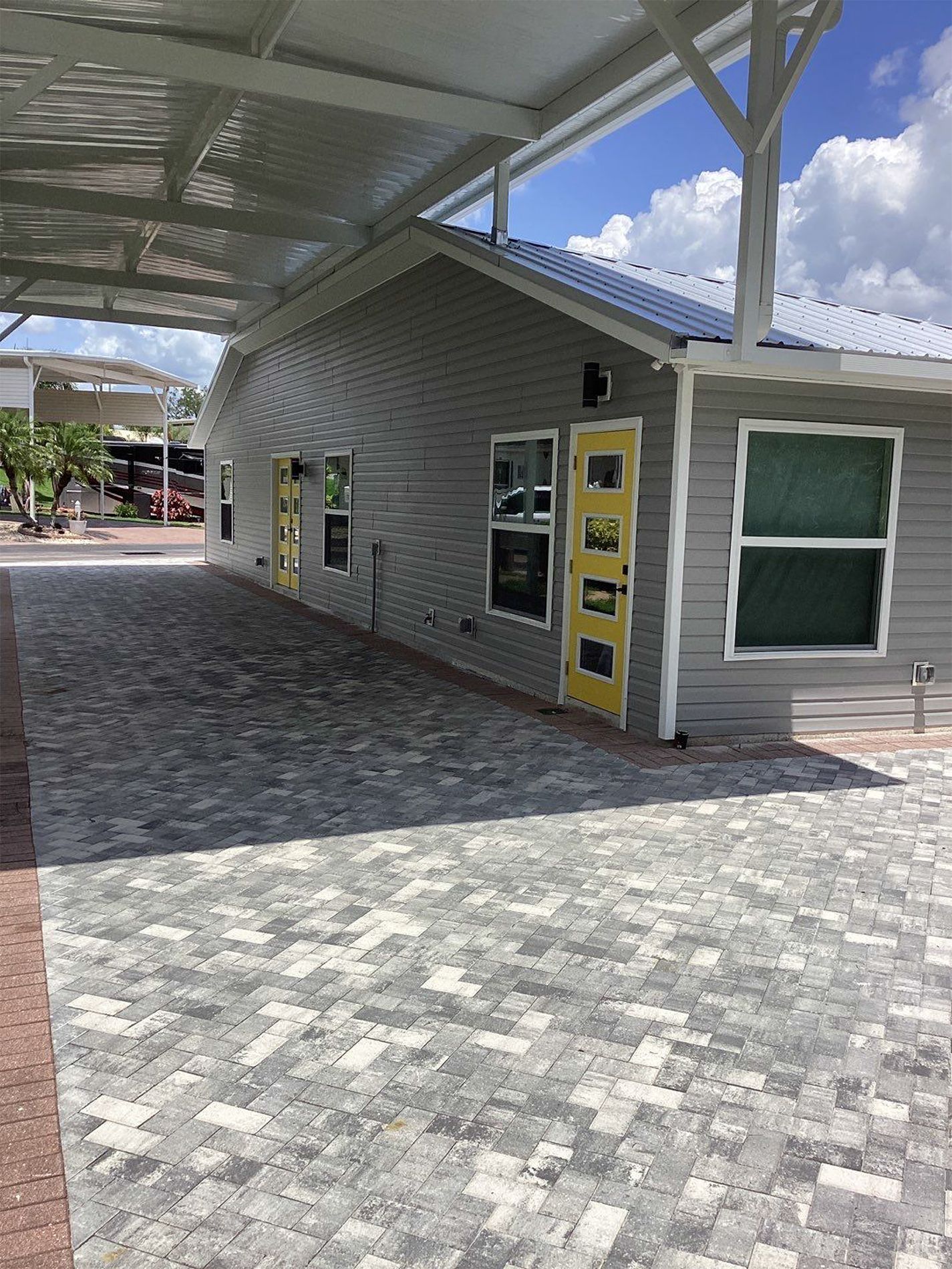 A gray house with a yellow door and a covered driveway.