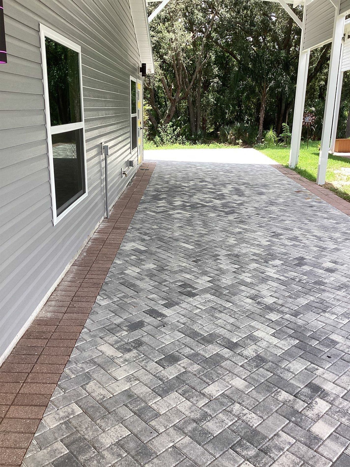 A brick driveway leading to a house with trees in the background.