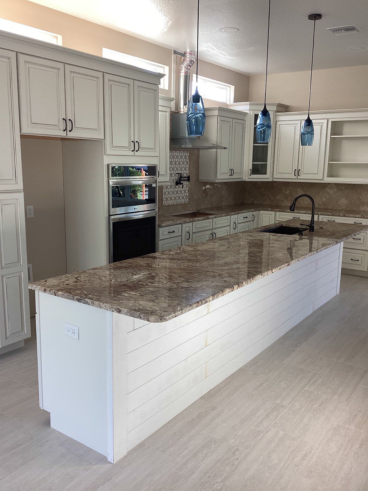 A kitchen with white cabinets , granite counter tops , and a large island.