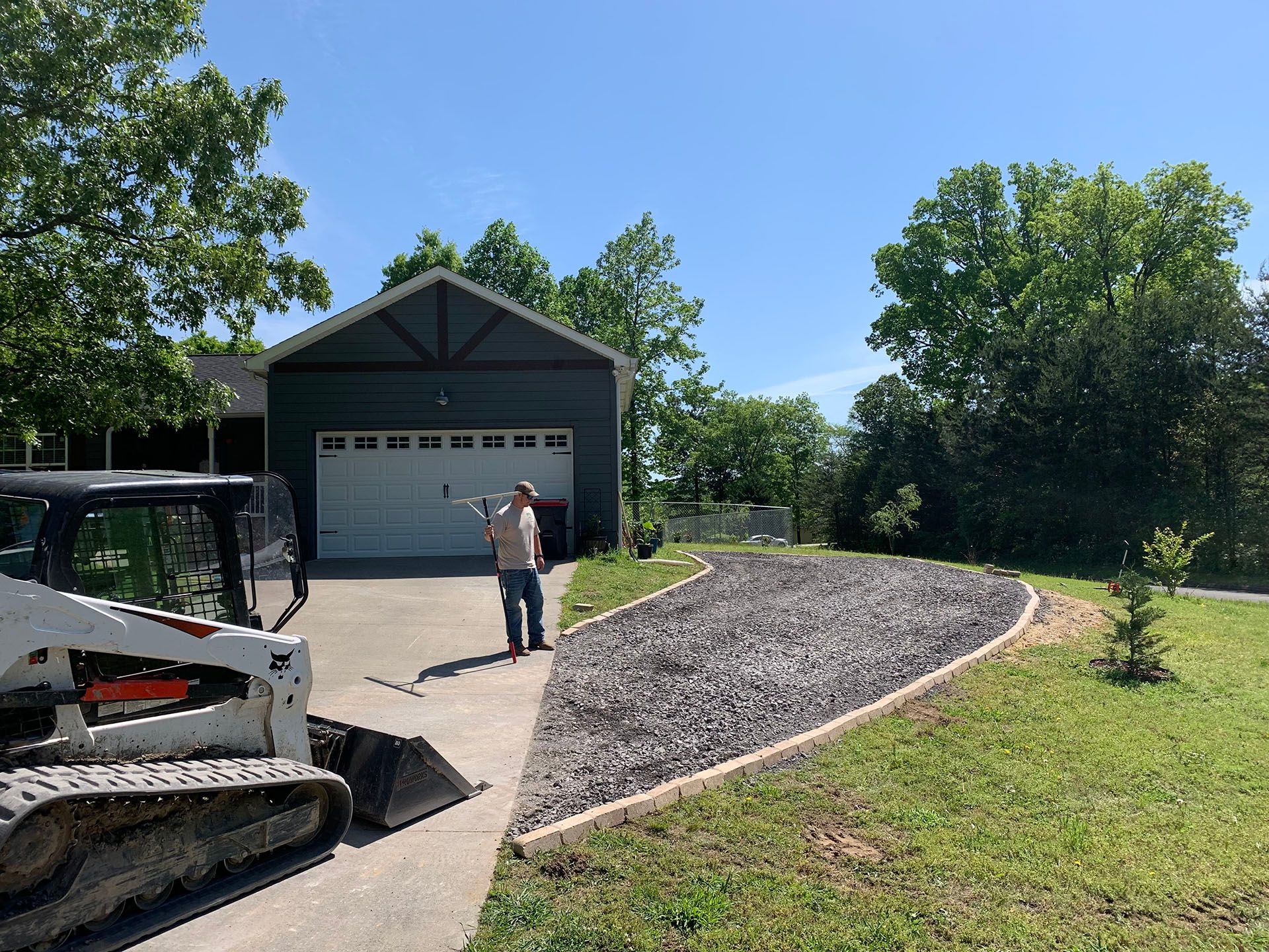 A man is standing in front of a house with a bulldozer in the driveway.