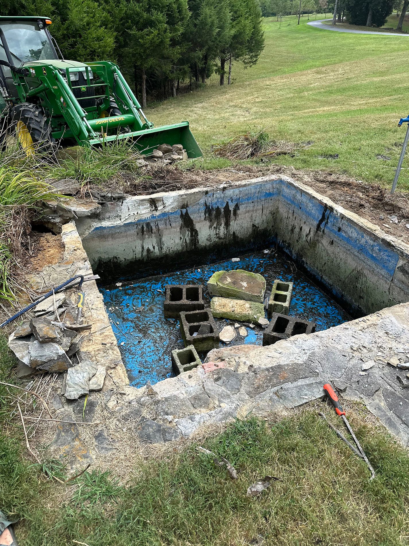 A tractor is digging a hole in the ground next to a swimming pool.