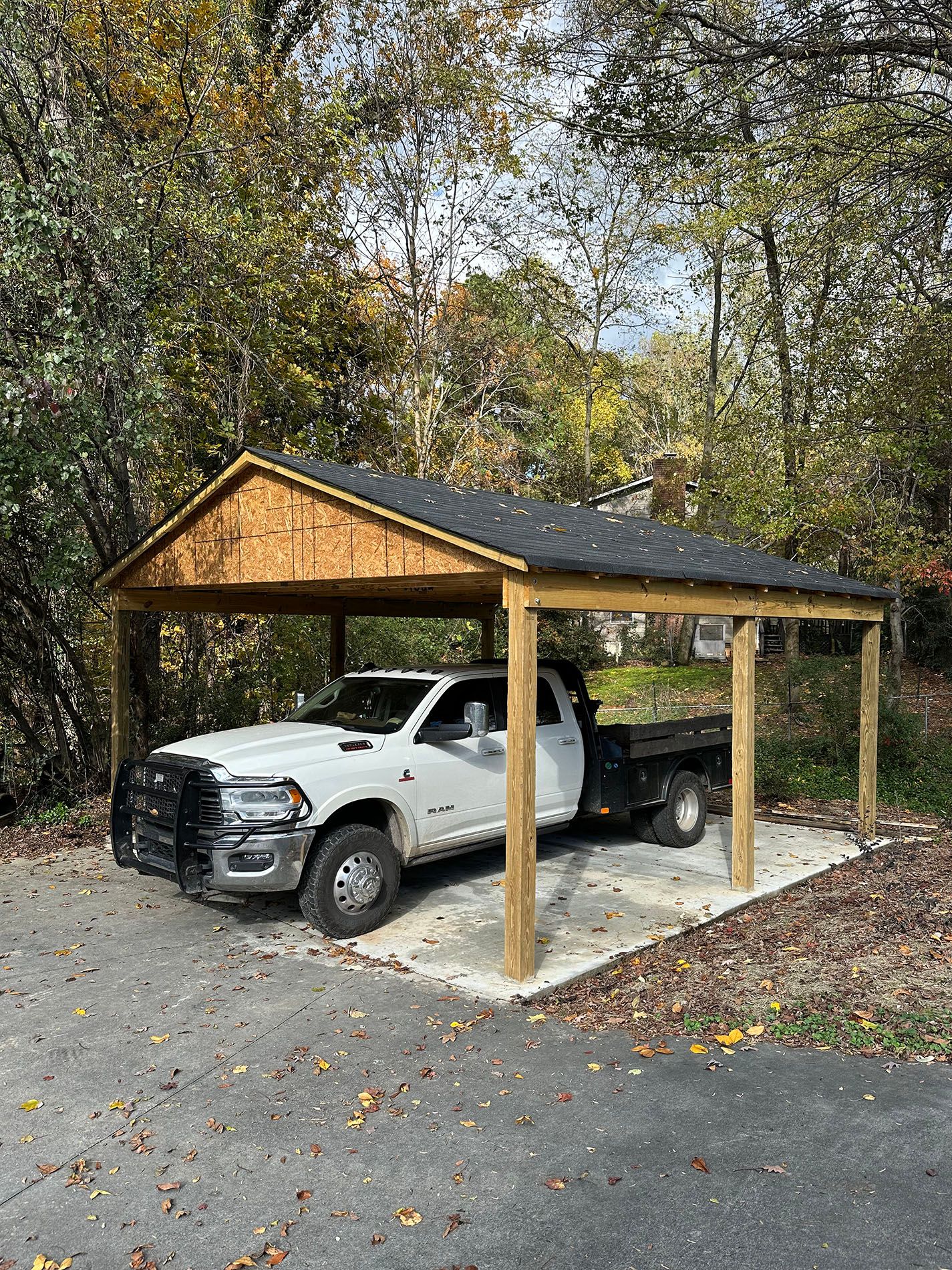 A white truck is parked under a wooden carport.