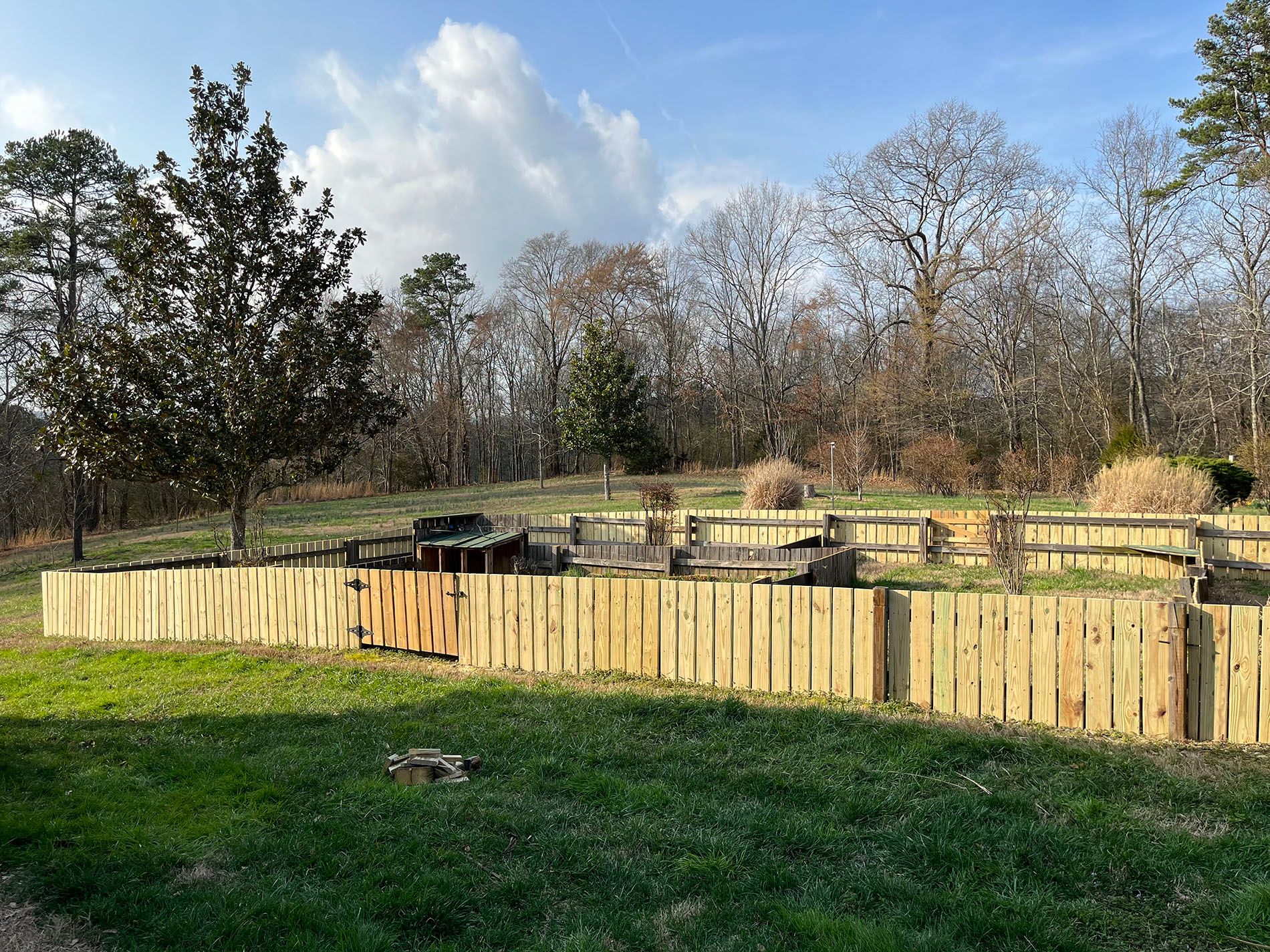 A wooden fence surrounds a grassy field with trees in the background.