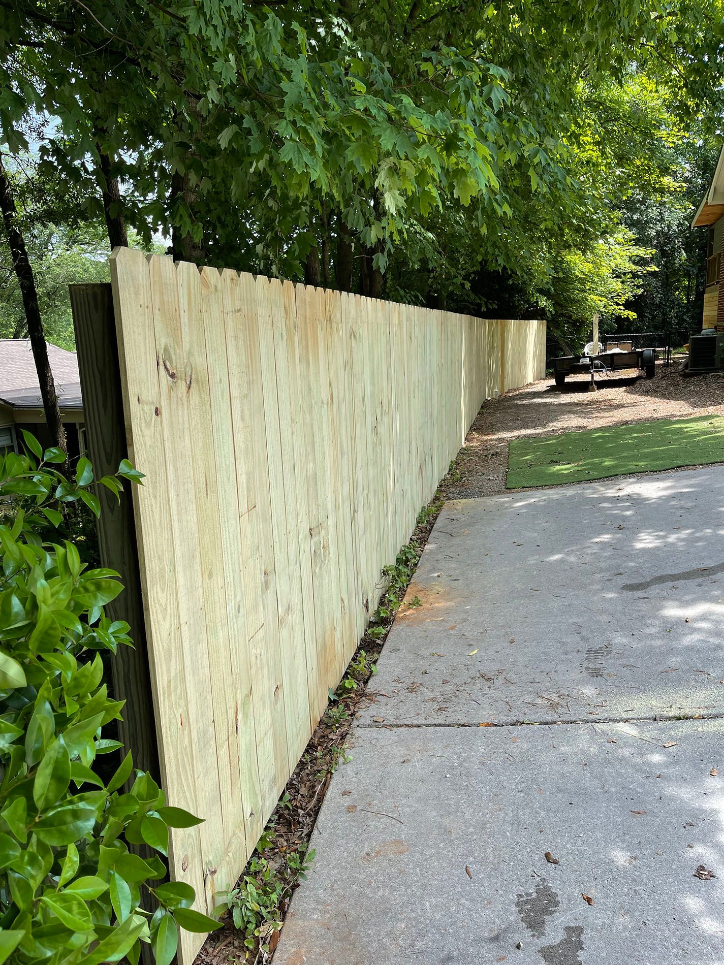 A wooden fence is sitting on the side of a sidewalk next to trees.