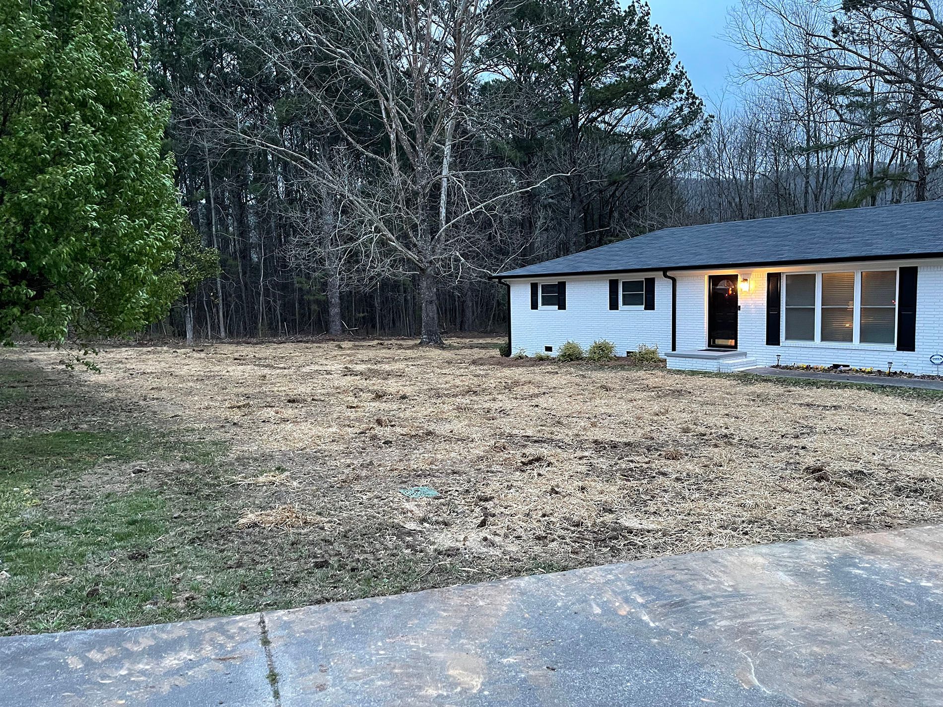 A white house with a black roof is sitting in the middle of a field surrounded by trees.