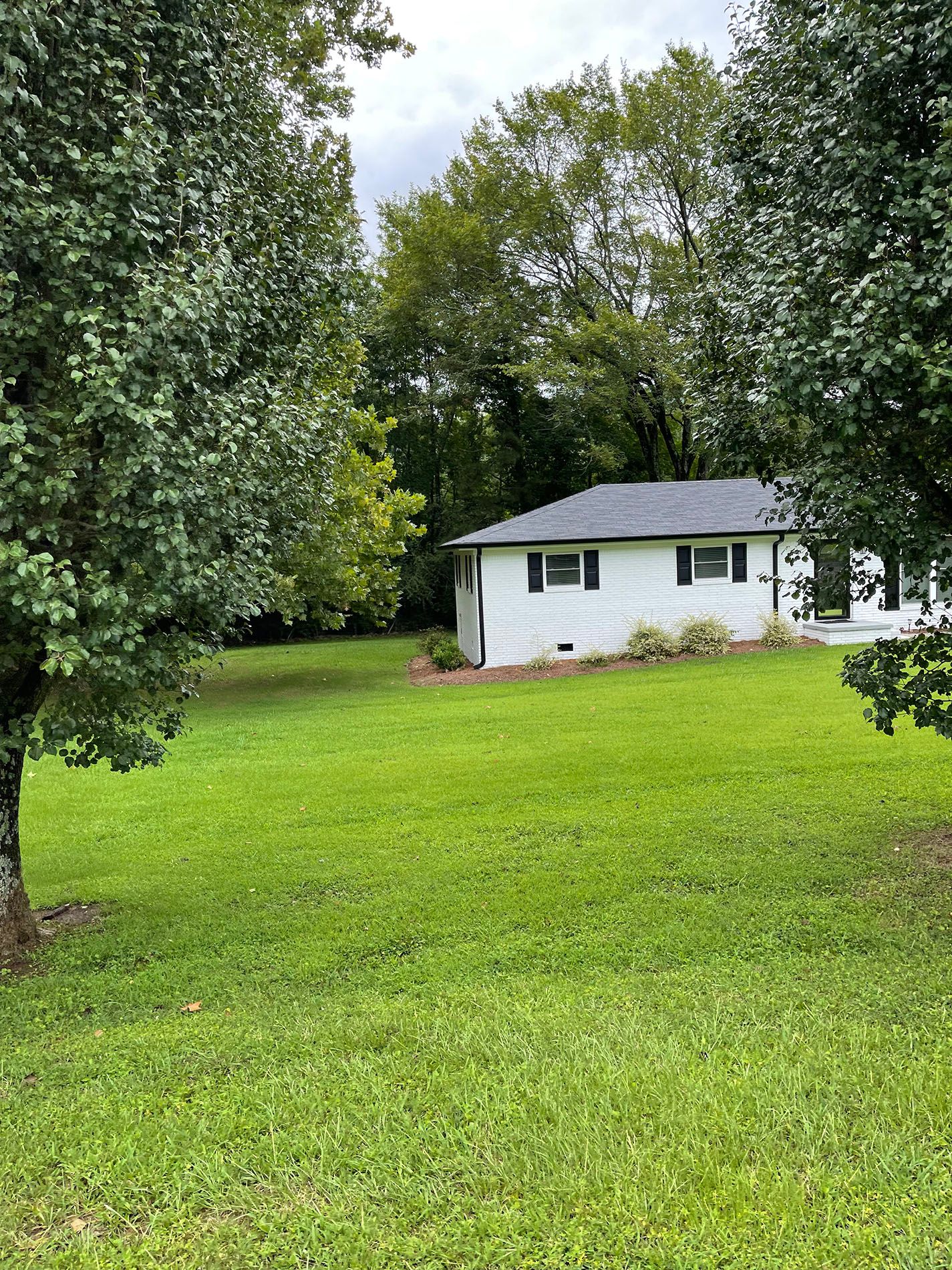 A white house is sitting in the middle of a lush green field surrounded by trees.
