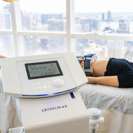 Person receiving cryoskin treatment, machine in foreground, window with city view in background.