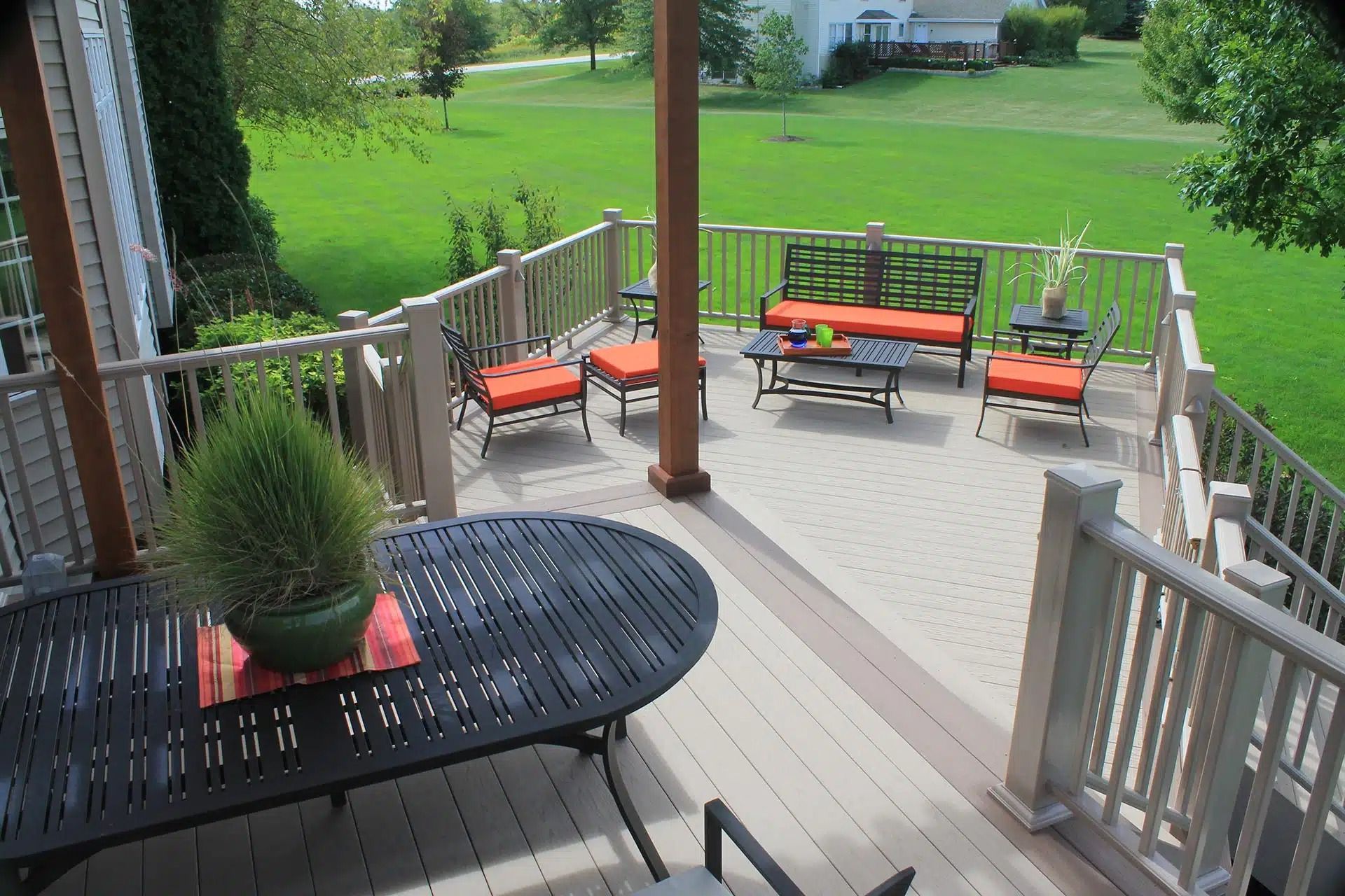Deck with outdoor furniture, lush green lawn in background. Orange cushions contrast with neutral tones.