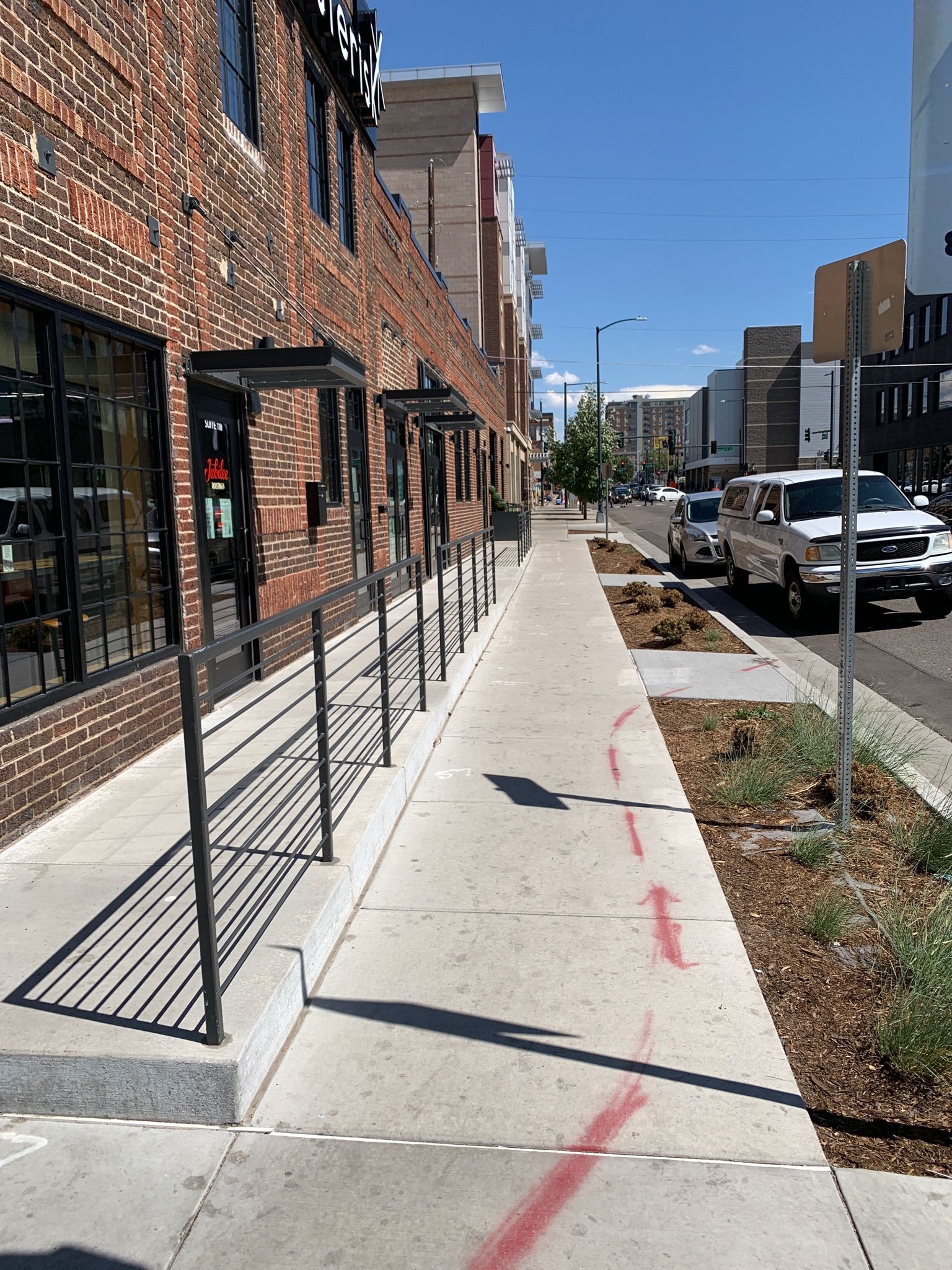 A sidewalk with orange cones and a green trash can.