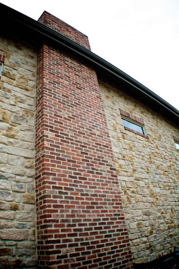 A large brick chimney is on the side of a stone building.