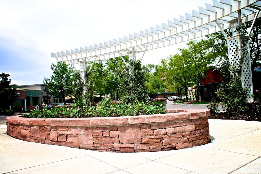 A stone wall with a planter in the middle of it under a white pergola.