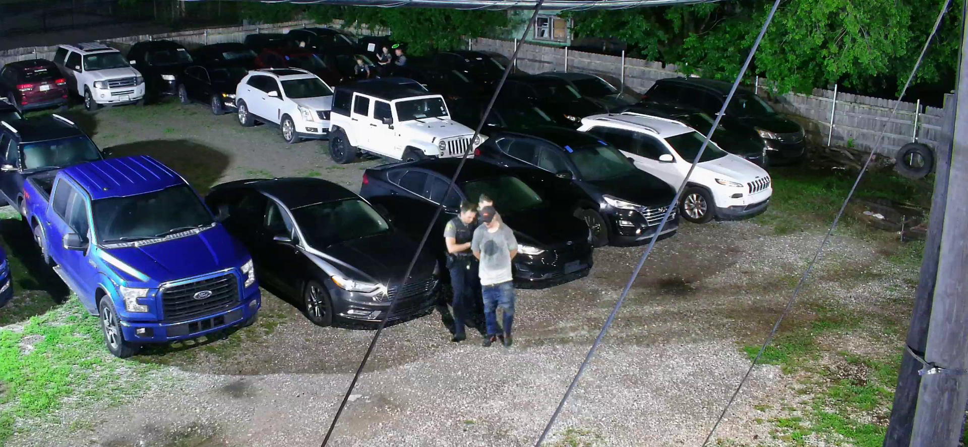 Nighttime parking lot with several parked cars and two people standing near a black car.