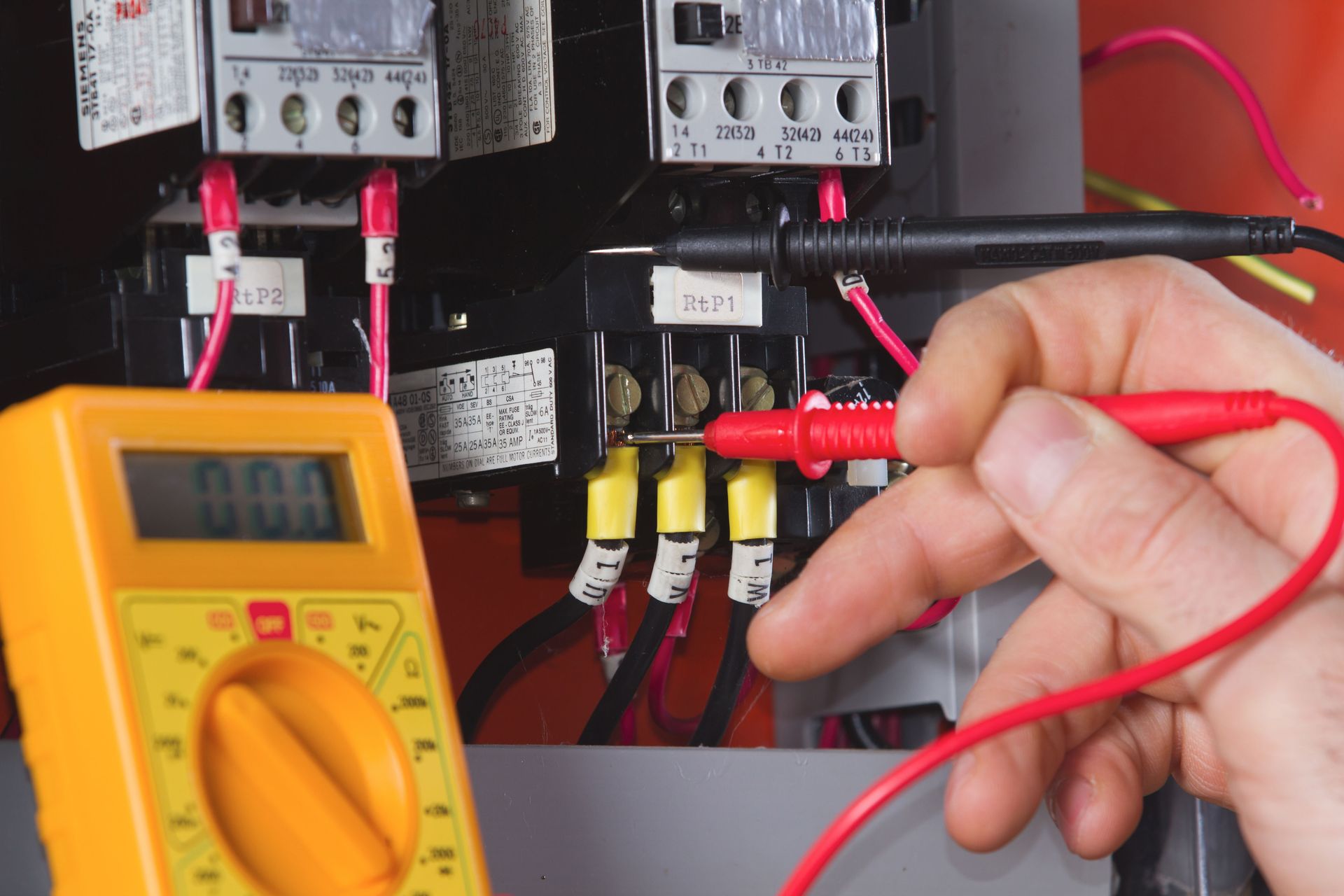 Person using a multimeter to test electrical wires inside a control panel.
