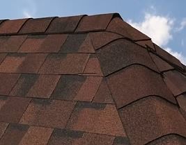 Close-up of a brown shingled roof corner against a blue sky with white clouds.