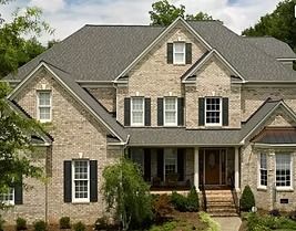 Two-story brick house with gray roof, black shutters, white trim, and a small front porch.