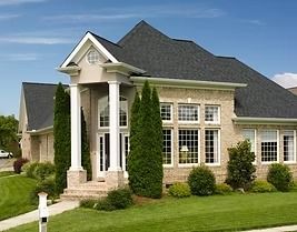 Beige brick house with dark roof, columns, large windows, and manicured lawn.
