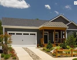 Single-story house with gray siding, white garage door, and small front porch under a bright blue sky.