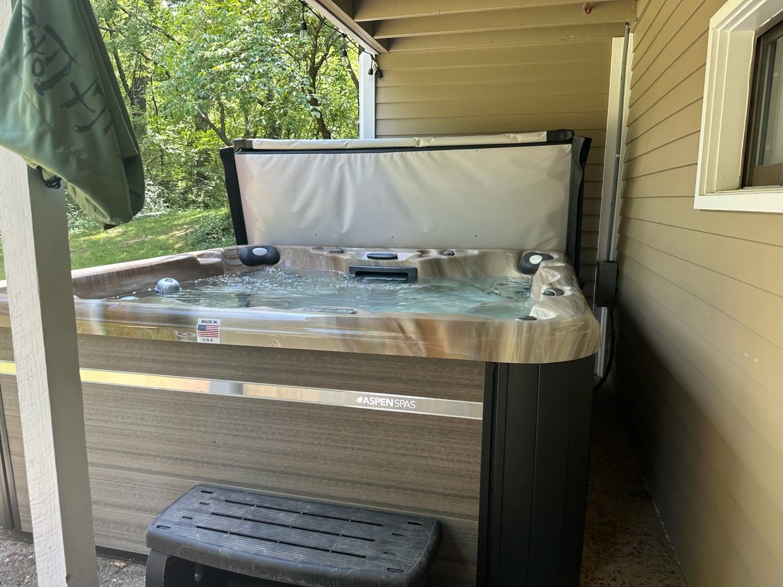 Hot tub with open cover on a porch next to a house. A step stool is in front.