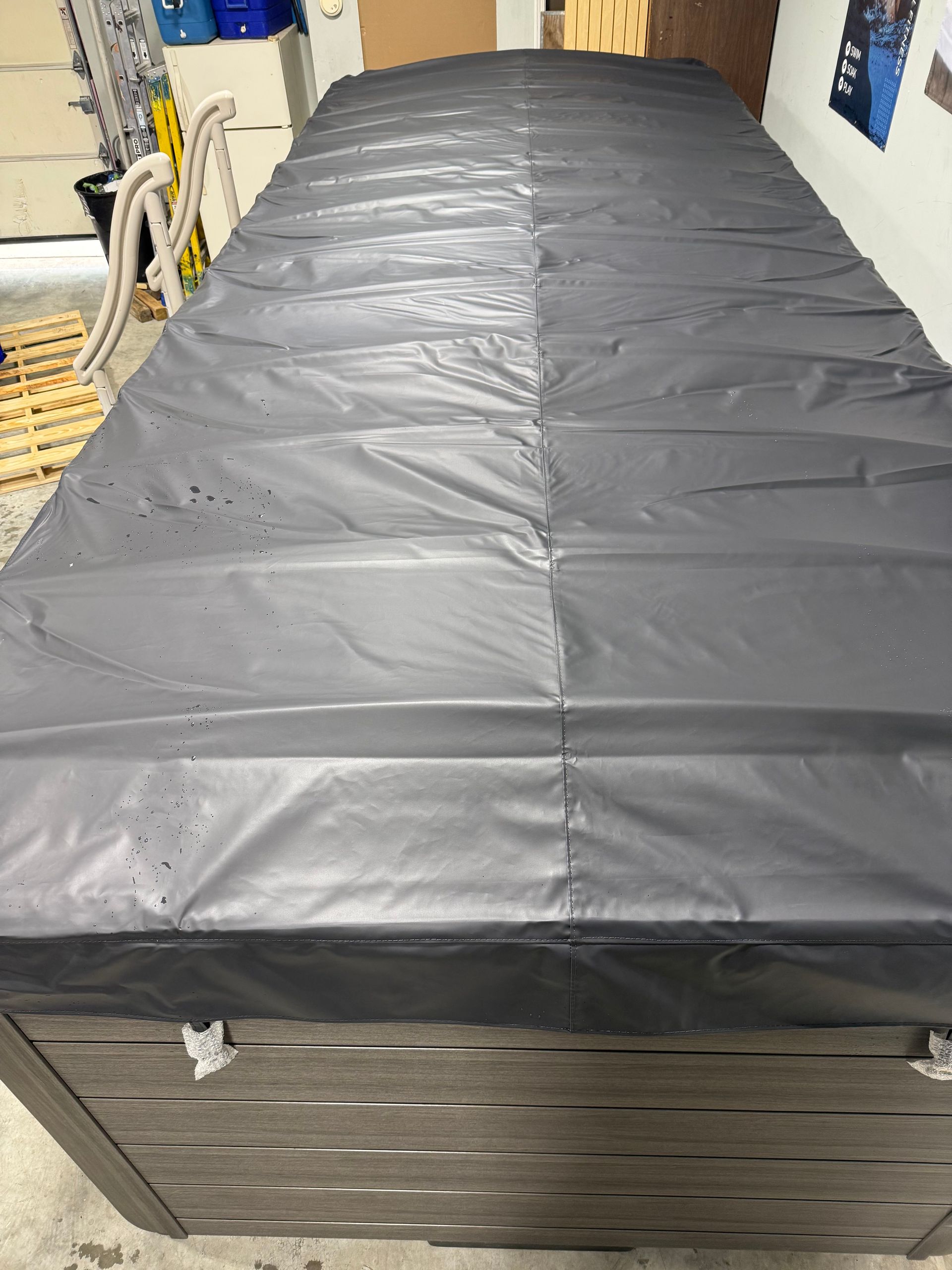 Dark gray hot tub cover on a gray wooden hot tub in a garage.