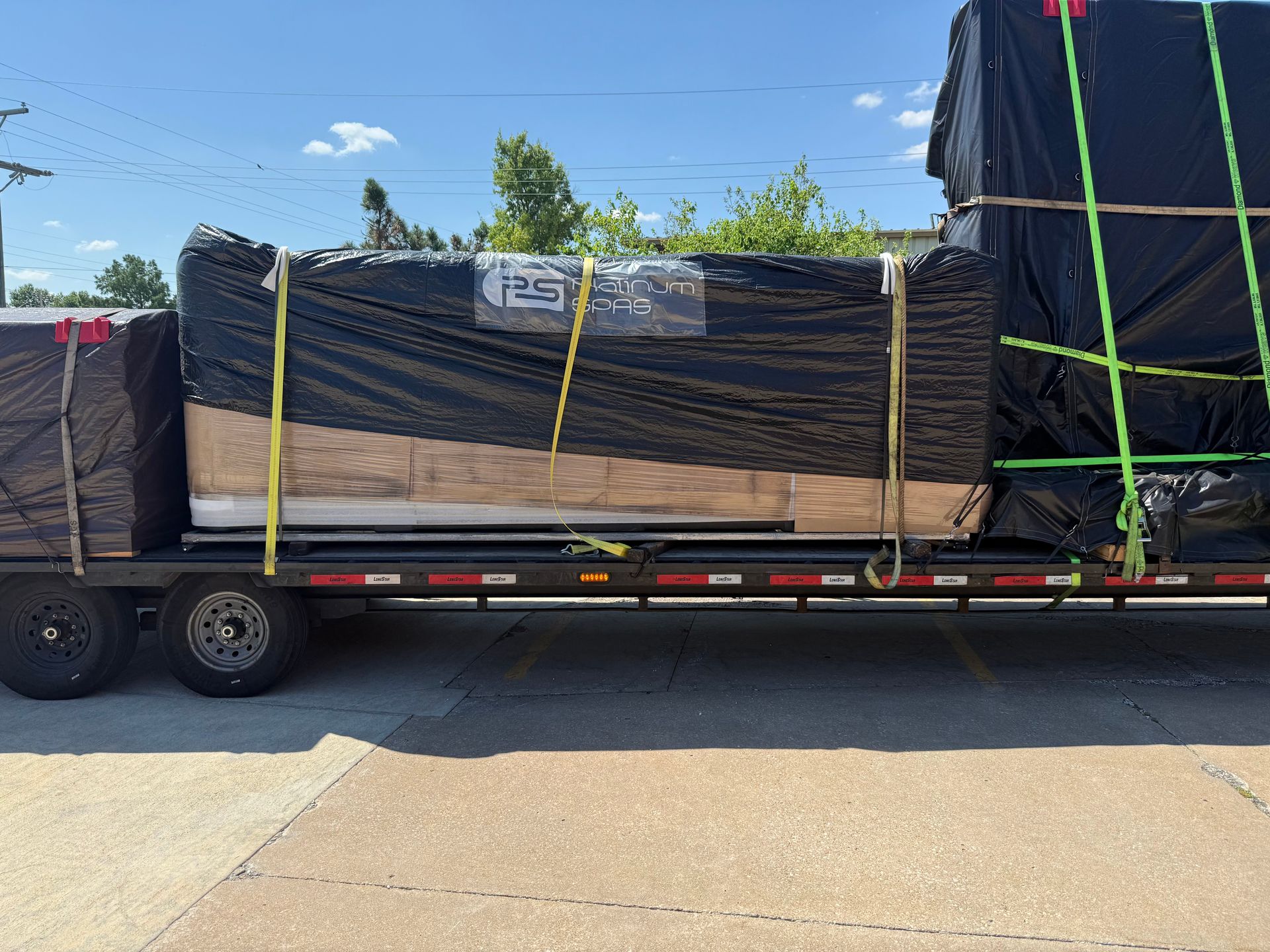 Flatbed trailer loaded with lumber wrapped in black plastic, secured with straps.
