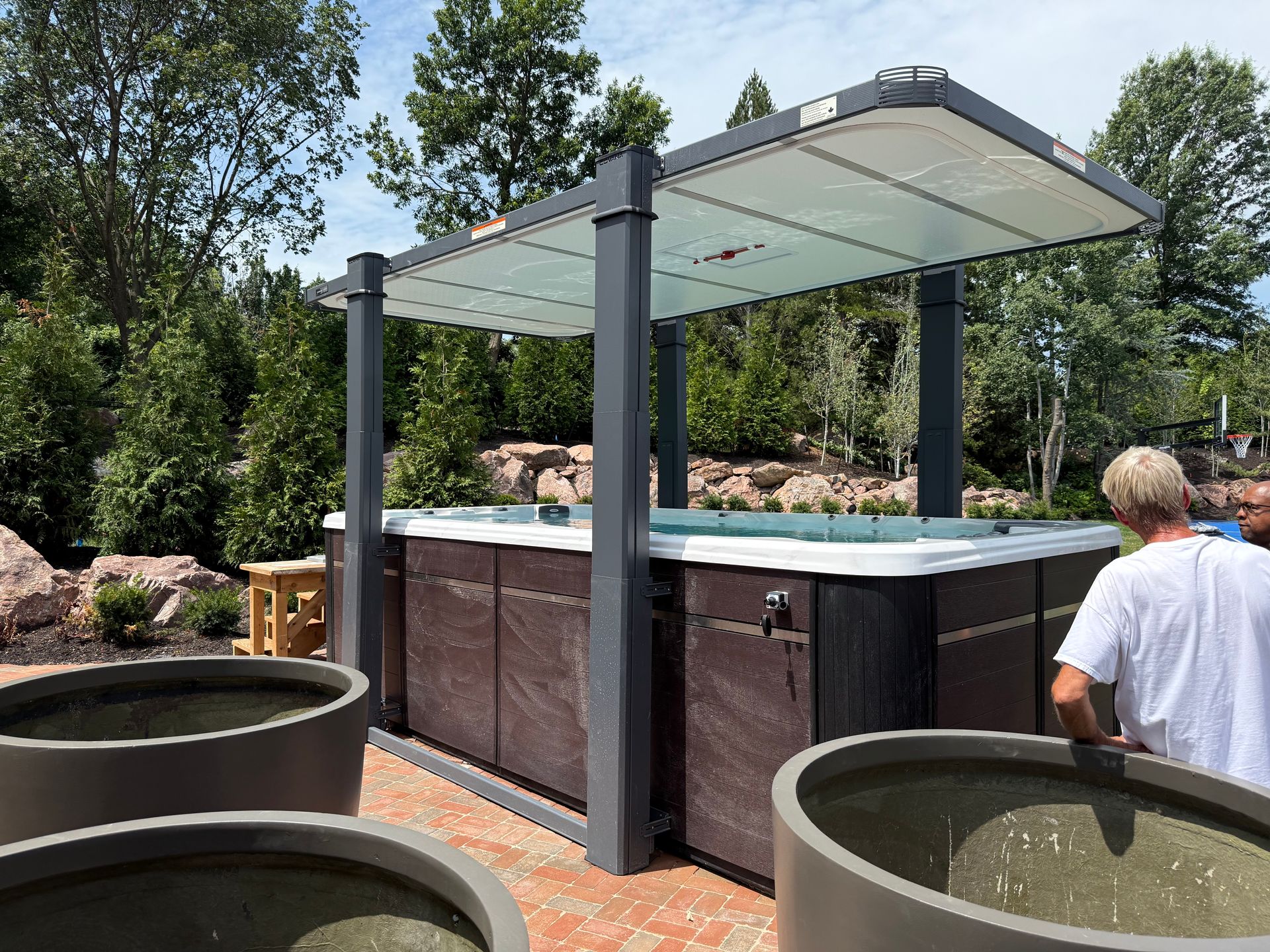 Hot tub with canopy in a yard. Man standing nearby. Gray planters in front.