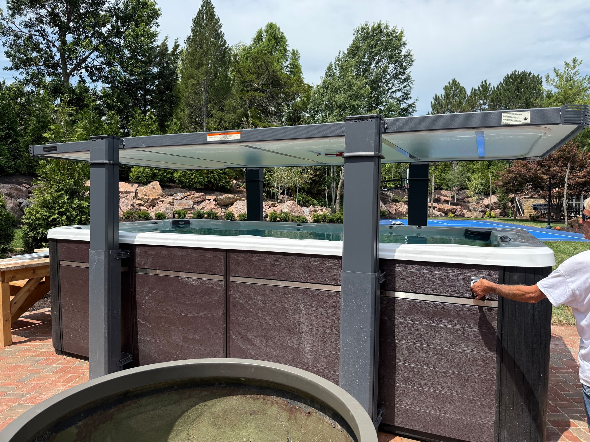 Hot tub with a retractable cover in an outdoor setting. Person reaching toward the cover.