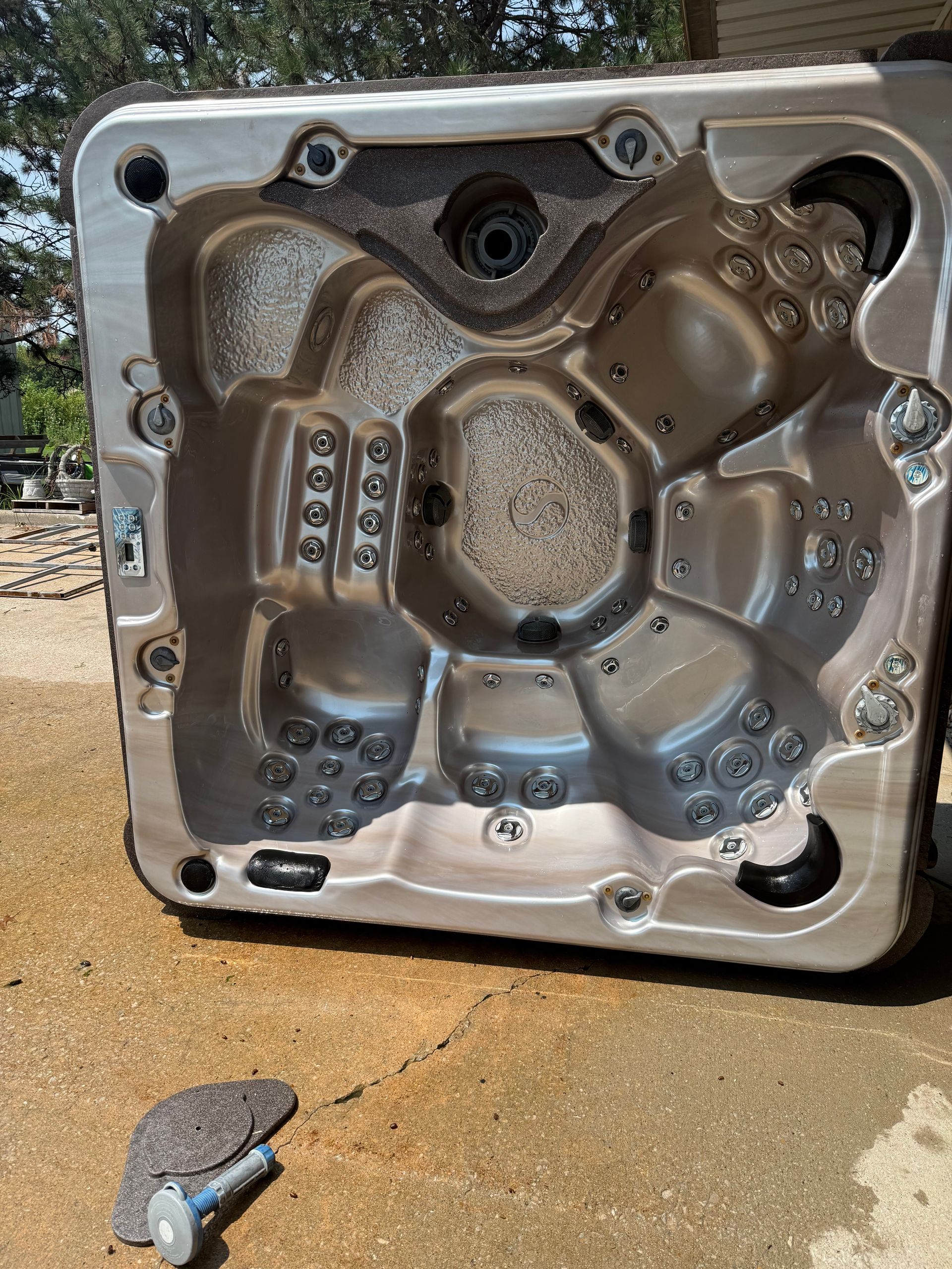 Empty, silver-toned hot tub basin on concrete, viewed from above. Jets and fittings are visible.