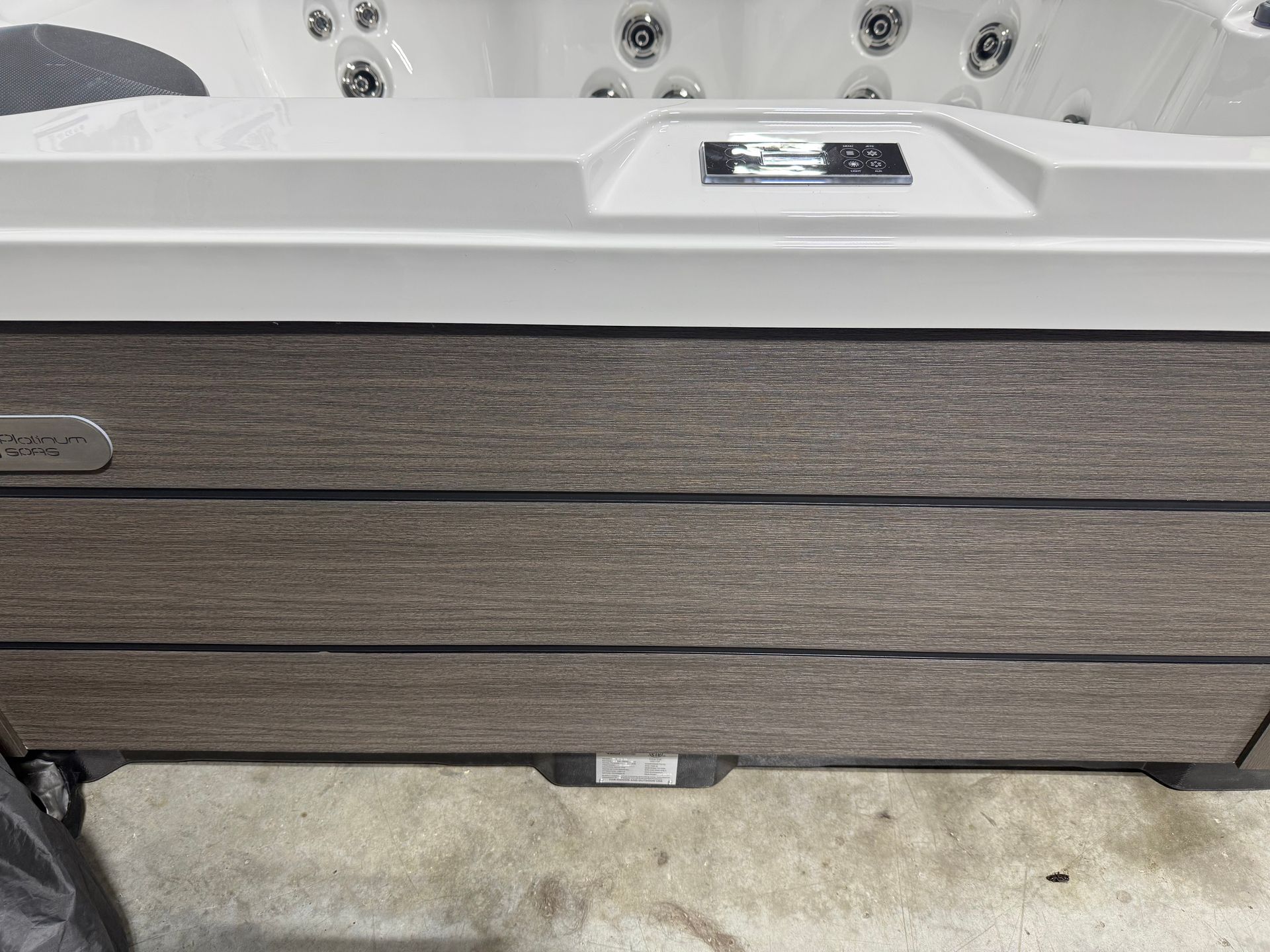 Hot tub exterior with gray wood-like paneling and a white top, on a concrete floor.