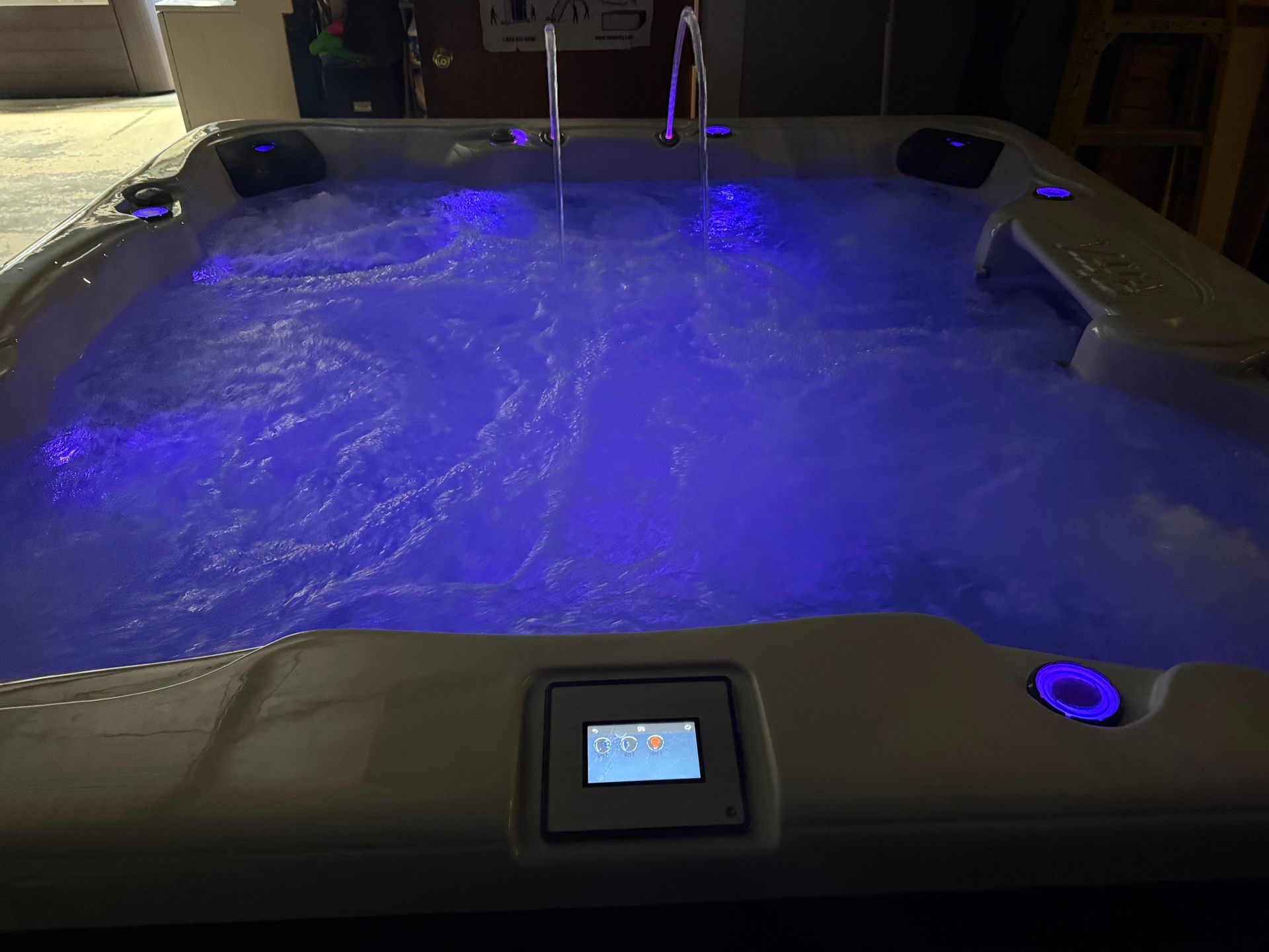 Lit-up jacuzzi with bubbling water; control panel visible. Blue interior lights, metal handrails.
