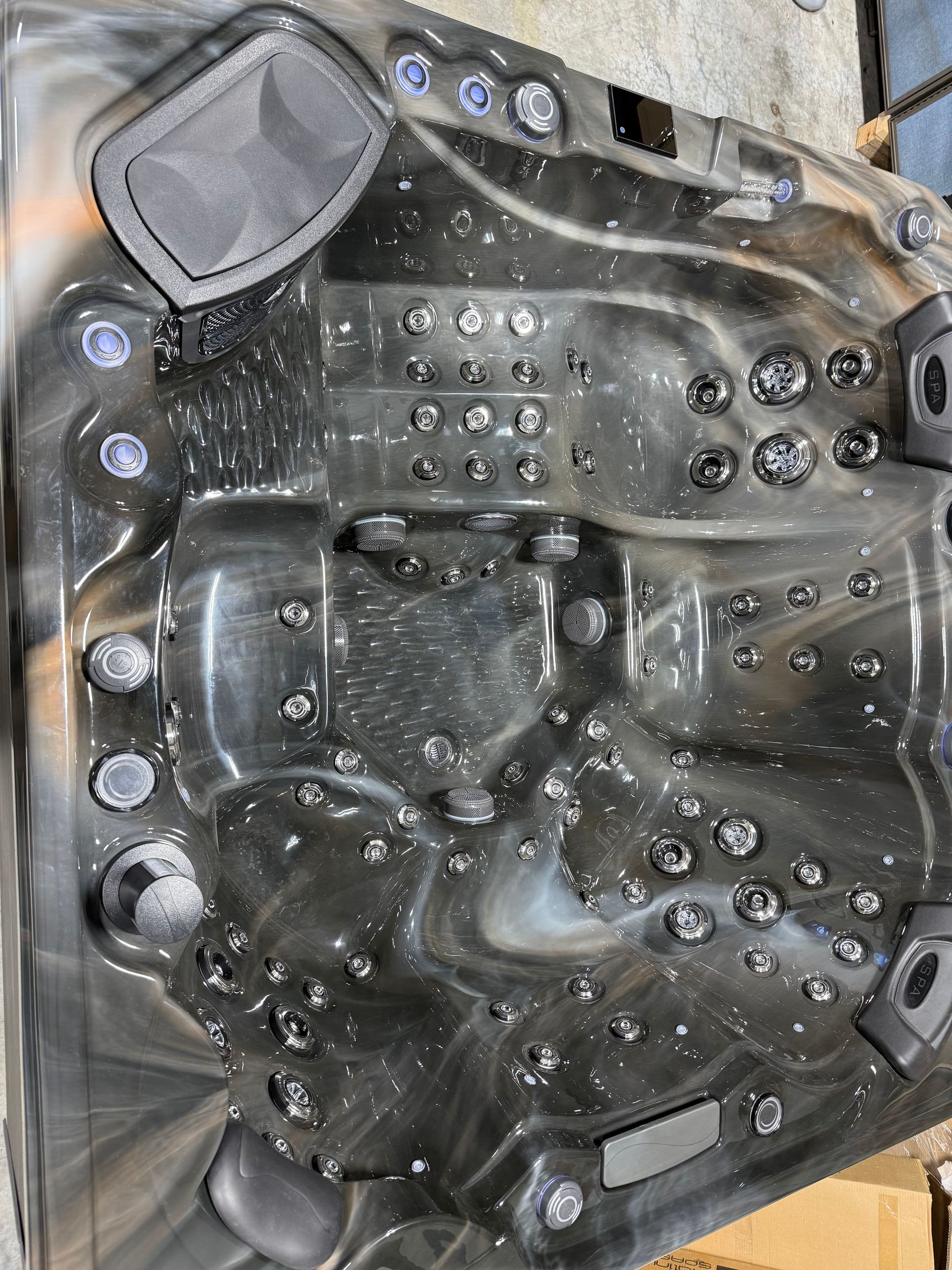 Dark-colored hot tub with many jets, control panel, and two speakers. Interior is gray, black, and white marbled.