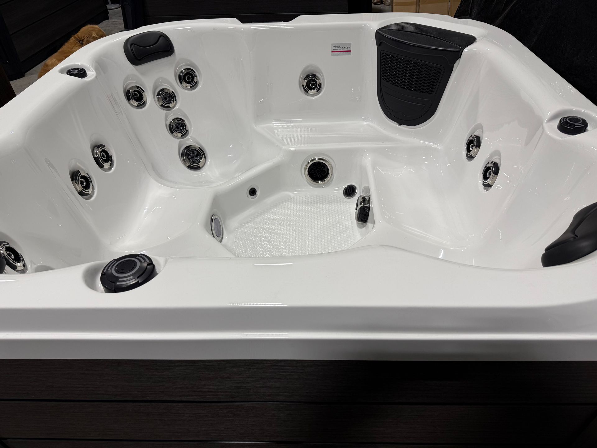 White hot tub with black jets, seating, and cover in a showroom setting.