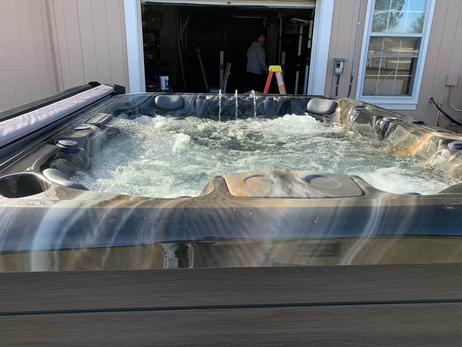 Hot tub with water jets, brown and white speckled surround, partially open garage in background.