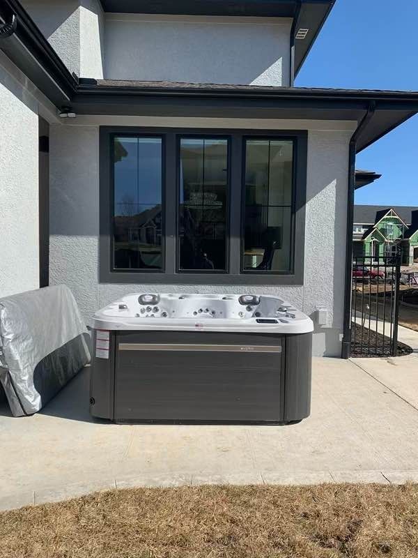Hot tub on patio near house with dark framed windows. Cover sits beside the tub.