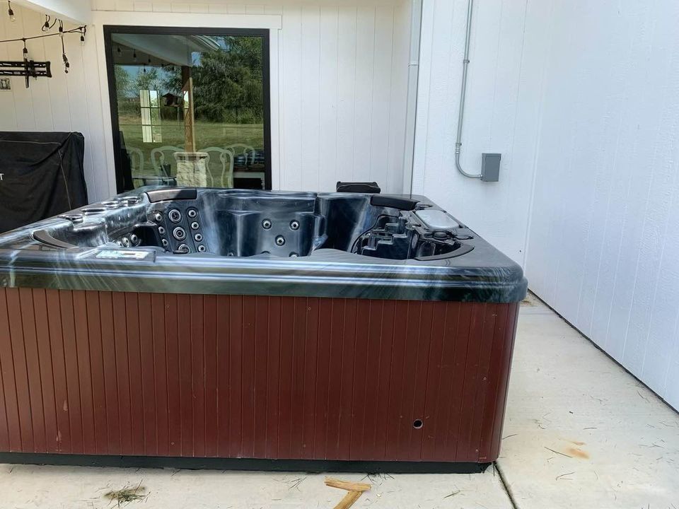 Hot tub, brown skirting, sits on concrete patio, near white wall.