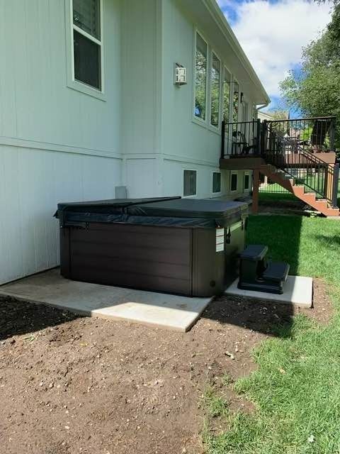 Hot tub with closed cover next to a house on a concrete pad. Deck and green grass in the background.