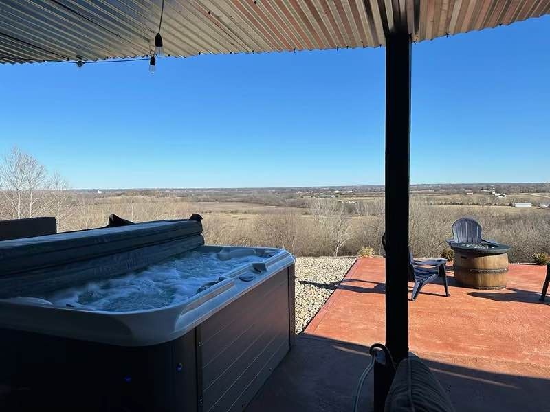 Hot tub on a patio overlooking a vast landscape under a blue sky, with seating nearby.