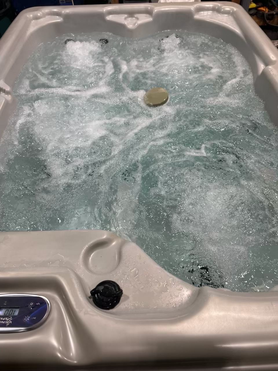 Bubbling hot tub with gray shell; water churning. A dark nozzle and a light-colored stone are visible.