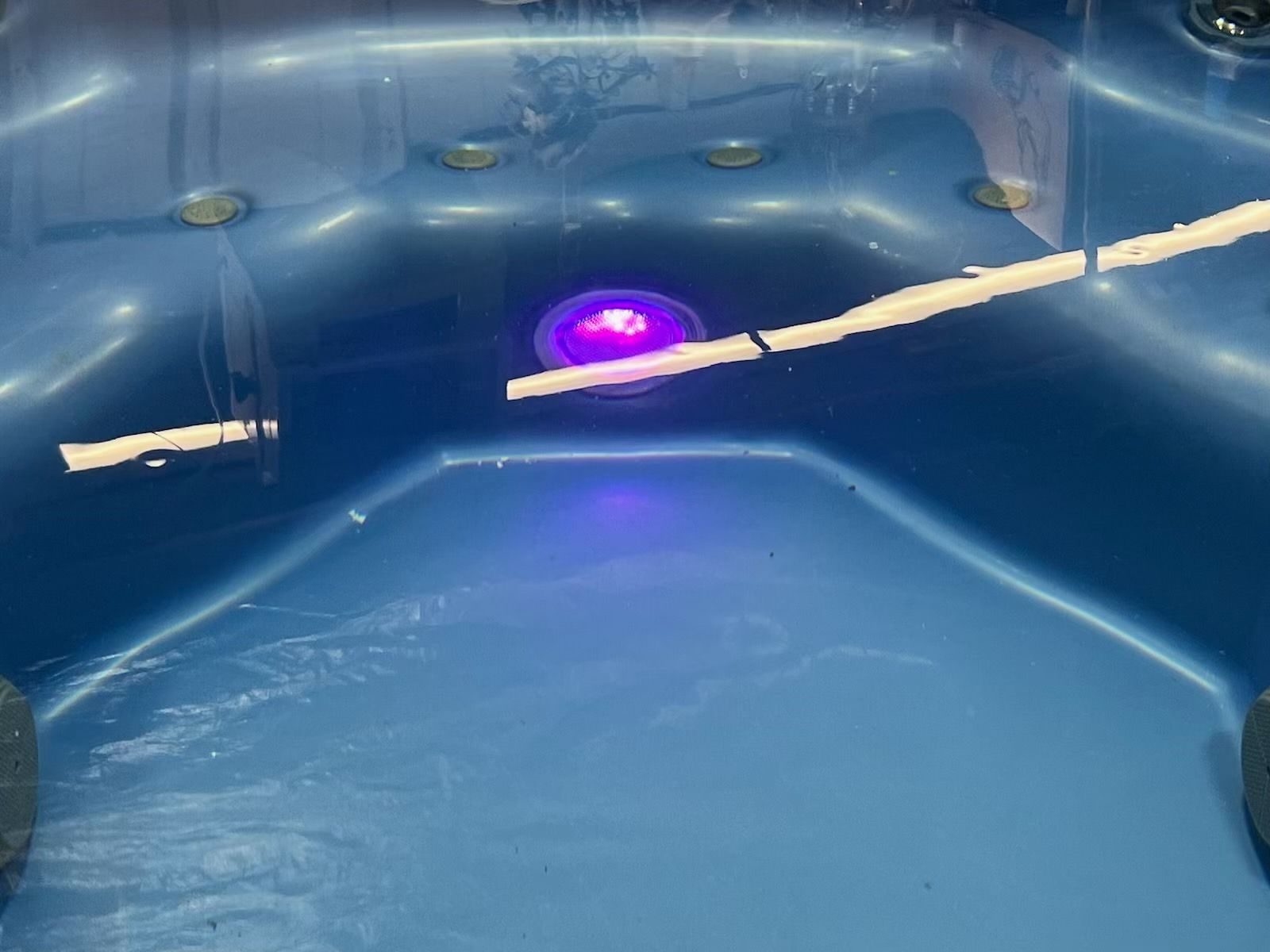 Blue hot tub with a central purple underwater light, a floating stick, and water marks.