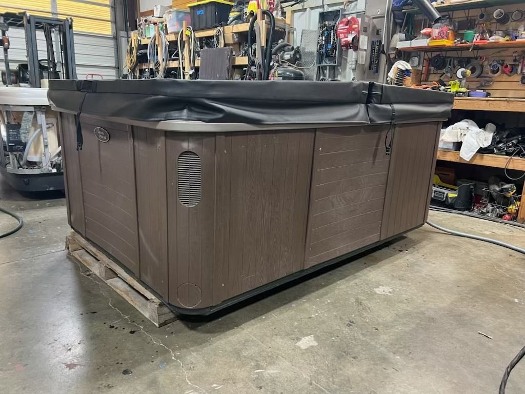 Brown hot tub with black cover on a pallet inside a garage.