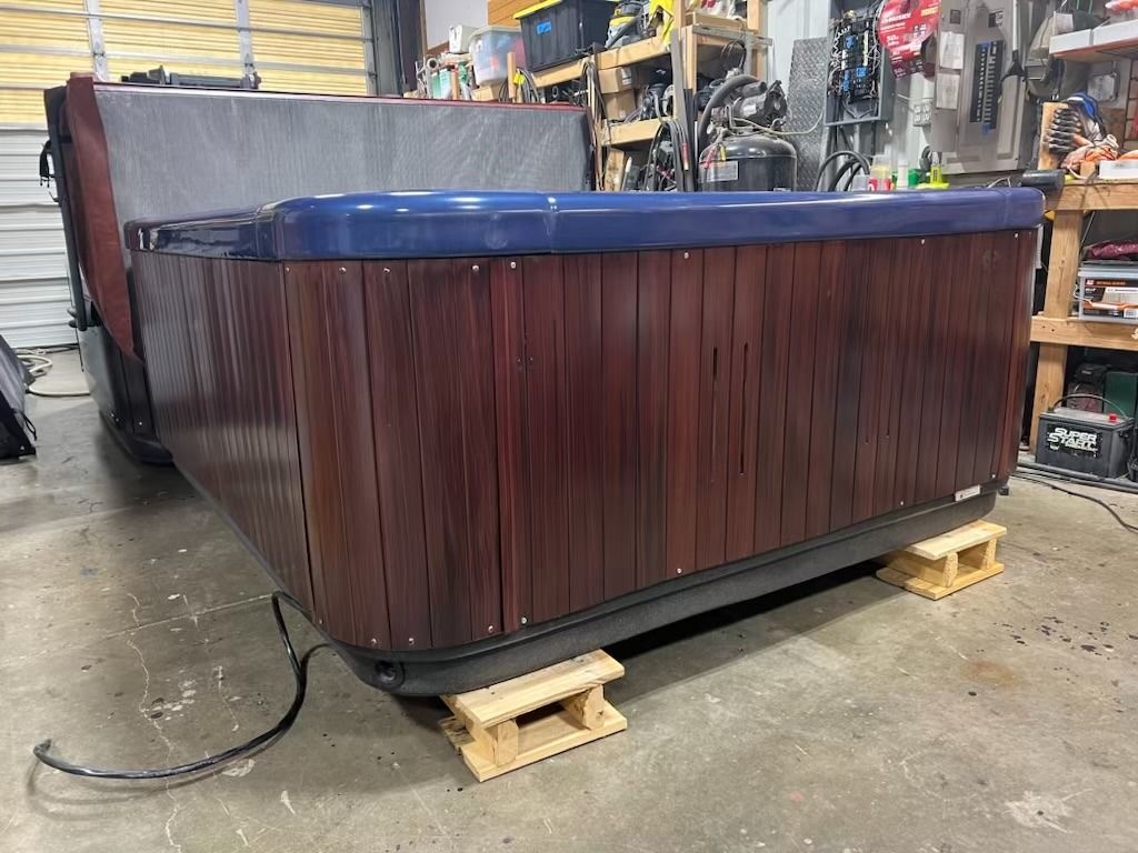 A hot tub with dark wood paneling, resting on wood blocks, with the cover partially open.