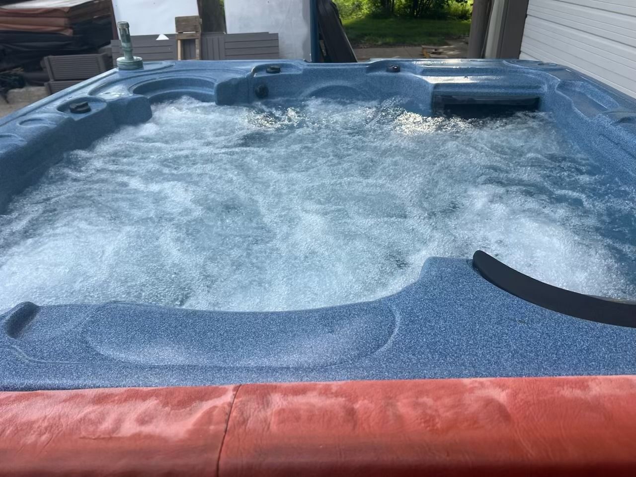 A hot tub with bubbly water, blue interior, orange-red trim, outdoors.