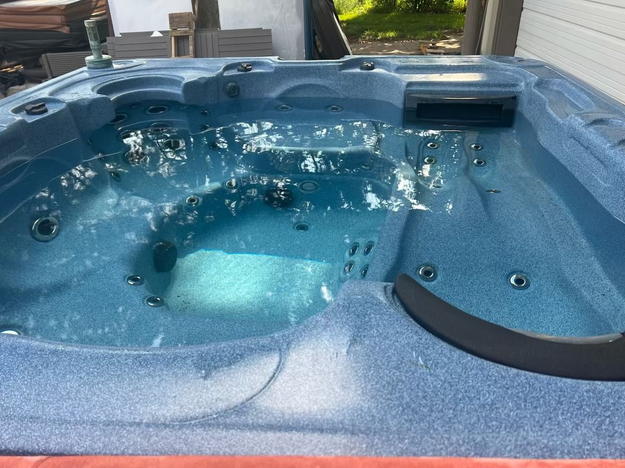 Blue hot tub filled with water, jets on, outdoors.