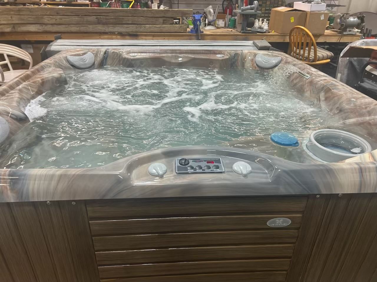 A hot tub filled with bubbling water, controls visible, in a workshop setting.