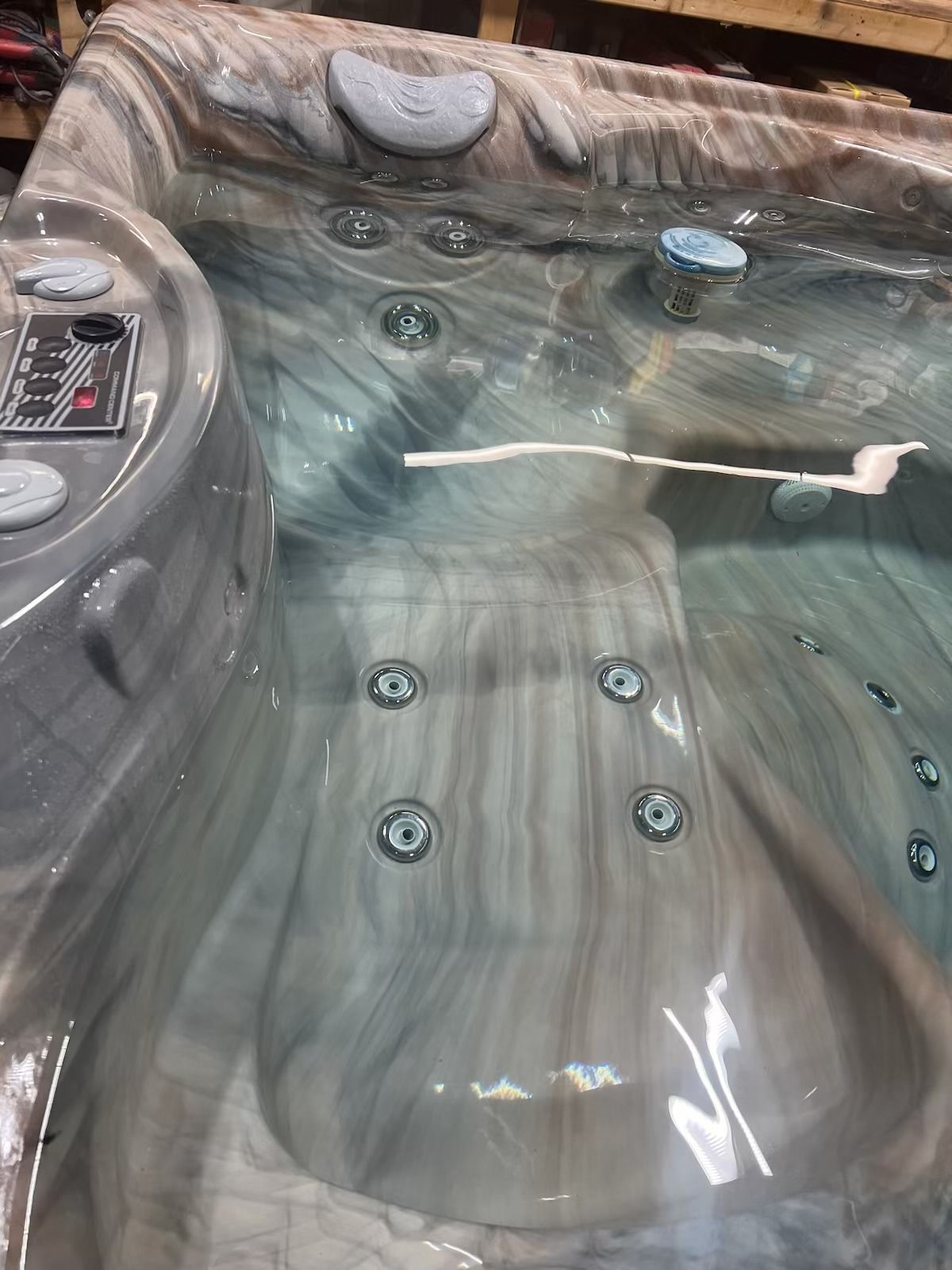 Hot tub interior with water, jets, control panel, and textured gray and white surface.