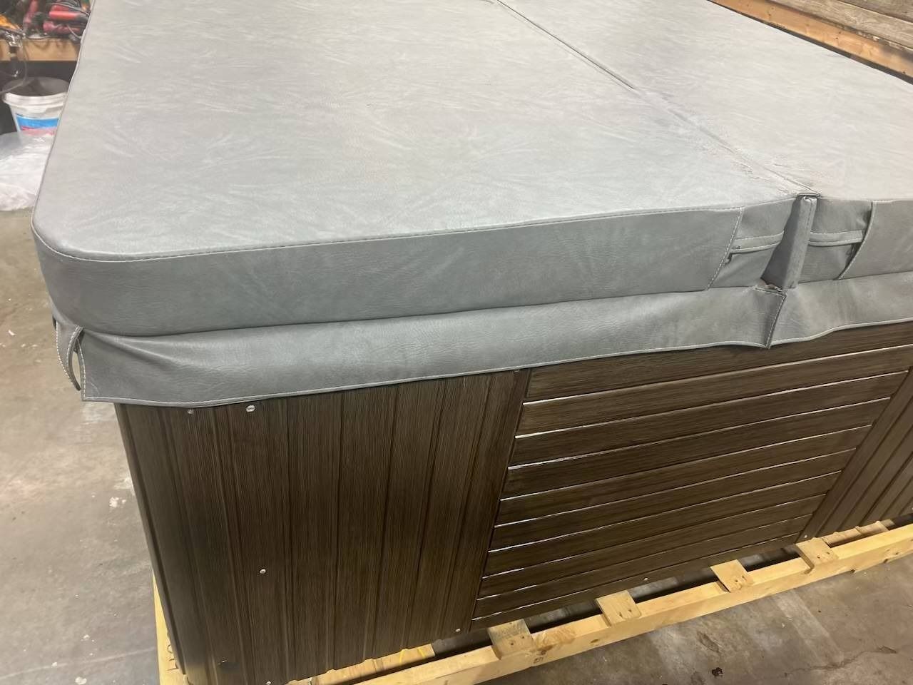 Hot tub with a gray cover, brown wooden siding, and sitting on a wooden pallet.