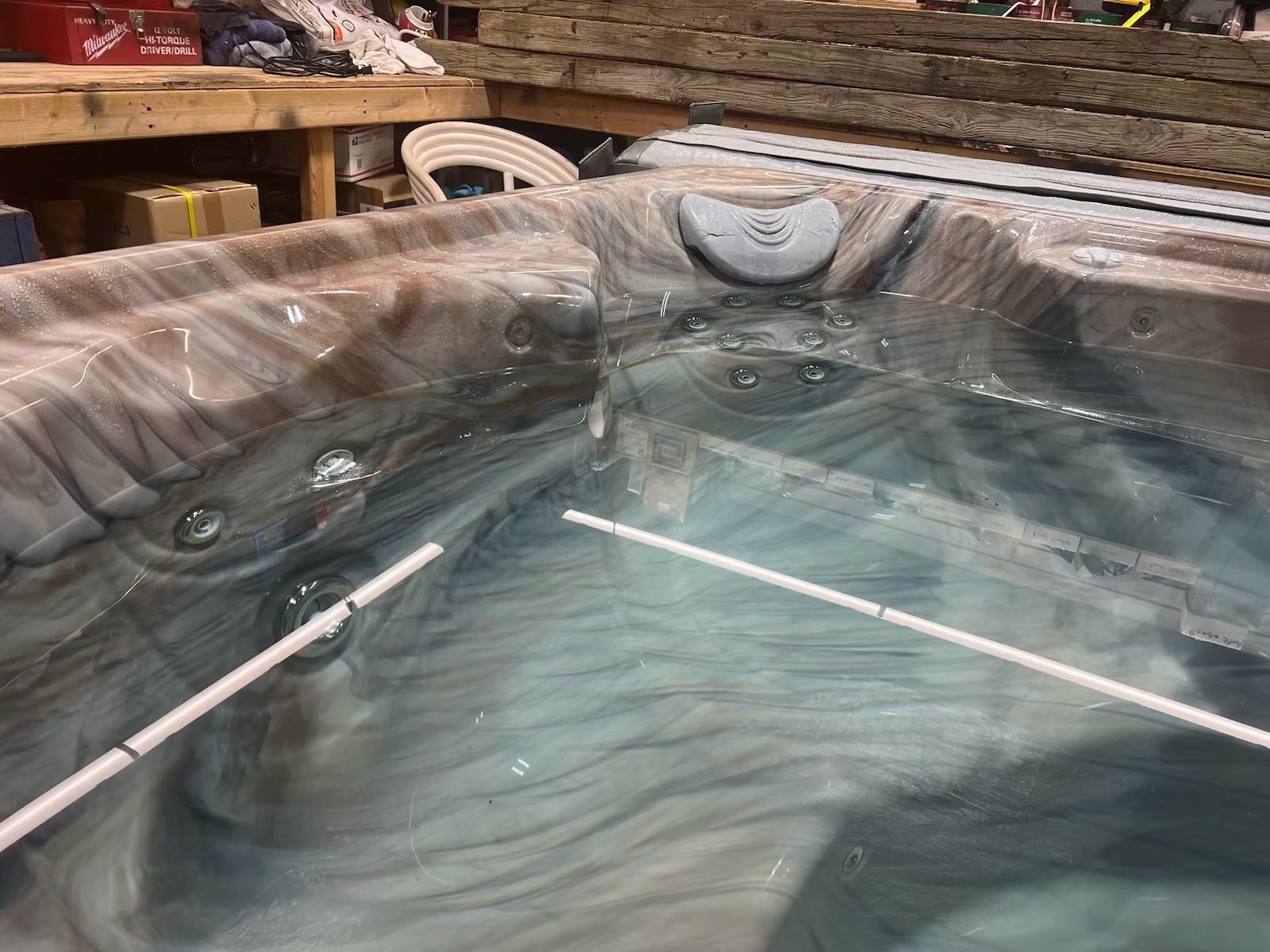 Hot tub filled with water, with jets and two white rods inside.